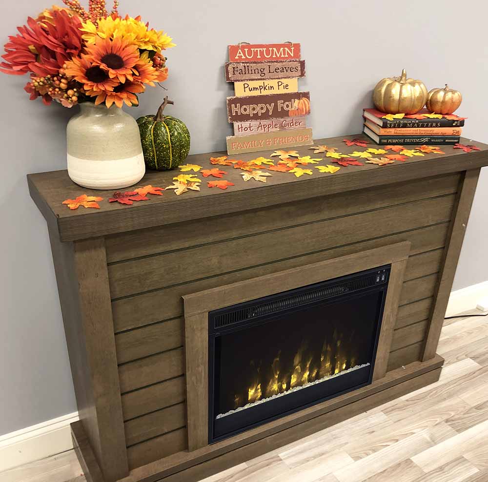 A shiplap wood wall mantel electric fireplace decorated with fall decor